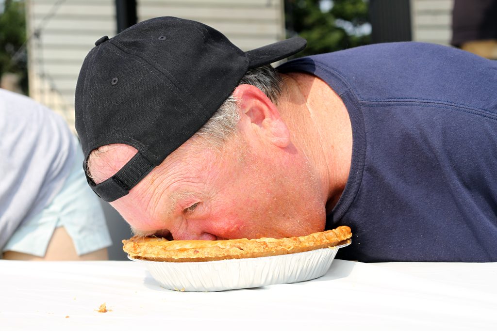 a guy with a baeball hat on backwards has his face in a pie tin, eating