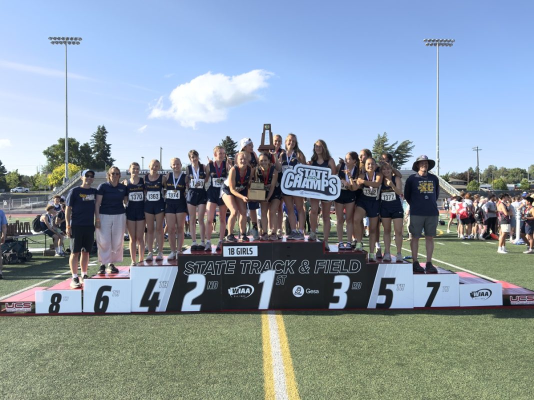 the girls track team in track shorts and jersey from Pope John Paul II High School stand on a podium with a a trophy and sign that says State Champs
