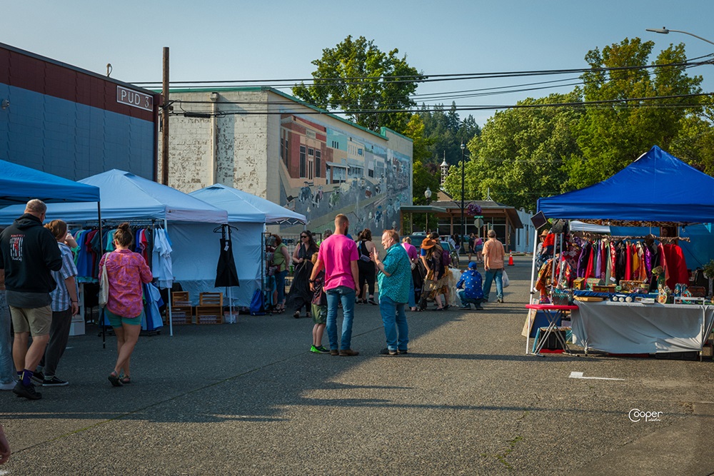 a large group of people mill around pop-up tents on a street in Shelton
