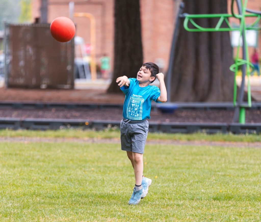 a kid in a t-shirt and shorts through a big red ball in a field