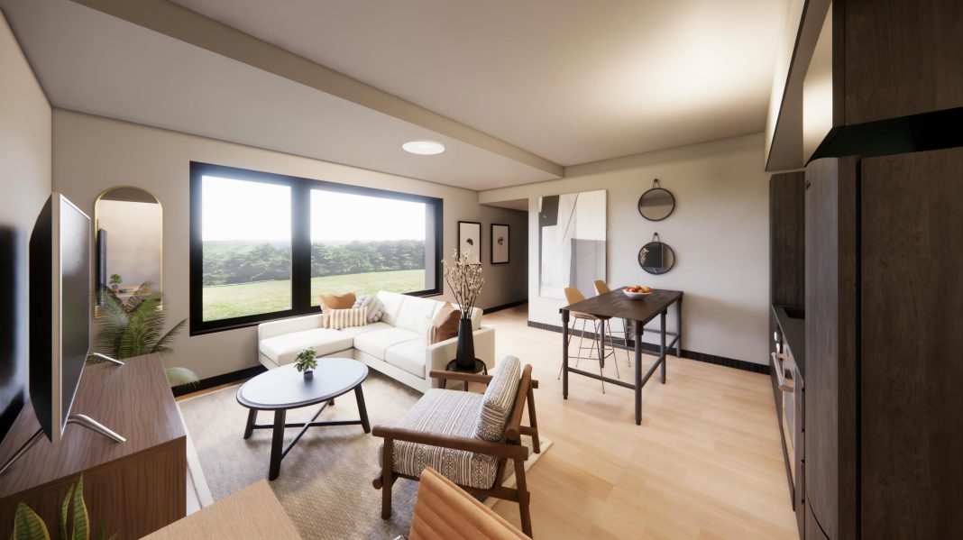 a living space at The Rookery with a kitchenette, a white couch, brown round coffee table and two table.. There is a window. A mirror and artwork are on the walls