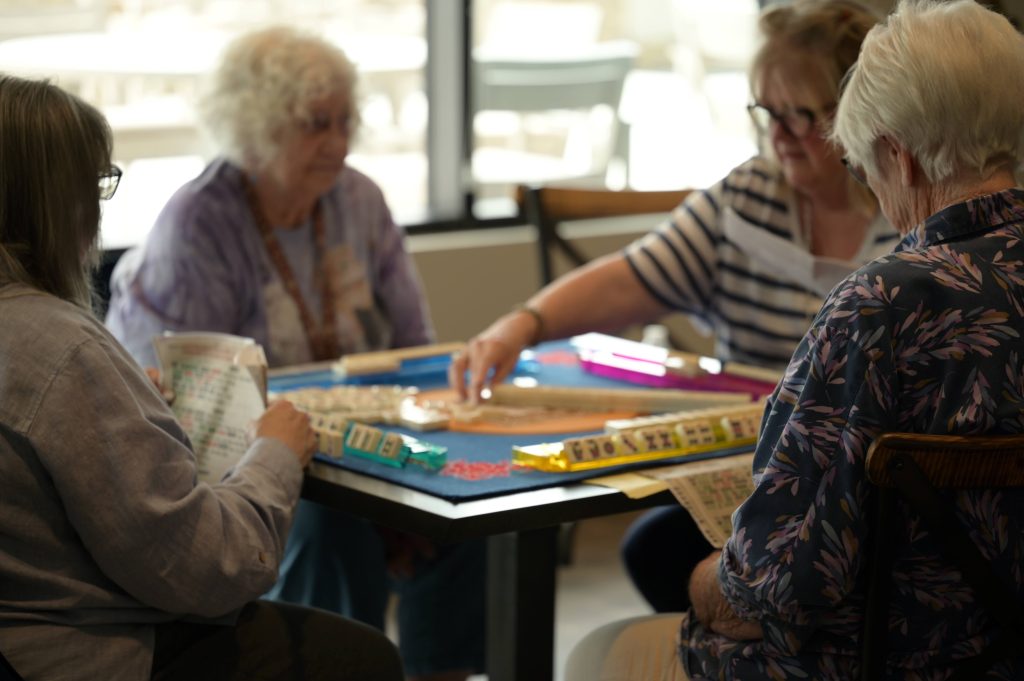 four senior citizens sitting at a square table playing a board game