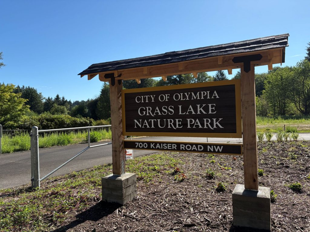 a wooden sign next to a metal arm gate says "City of Olympia Grass Lake Nature Park. 700 Kaiser Road NW"