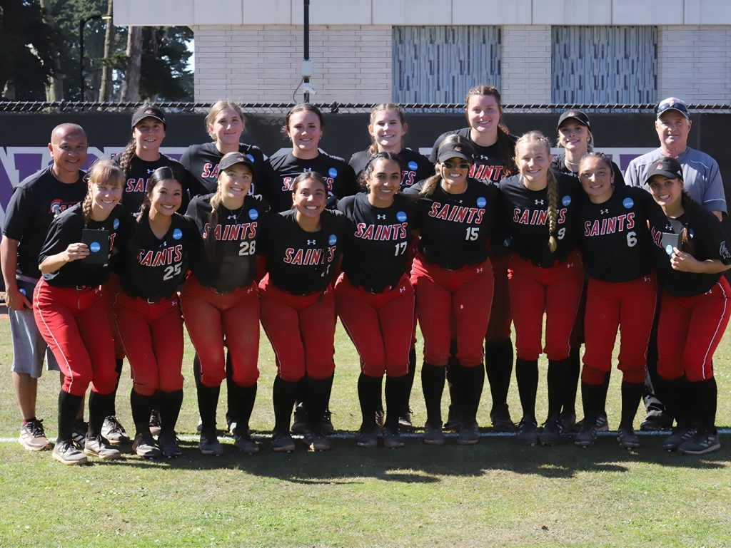 Saint Martins Softball team in black and red uniforms posing for a team photo with their coach.