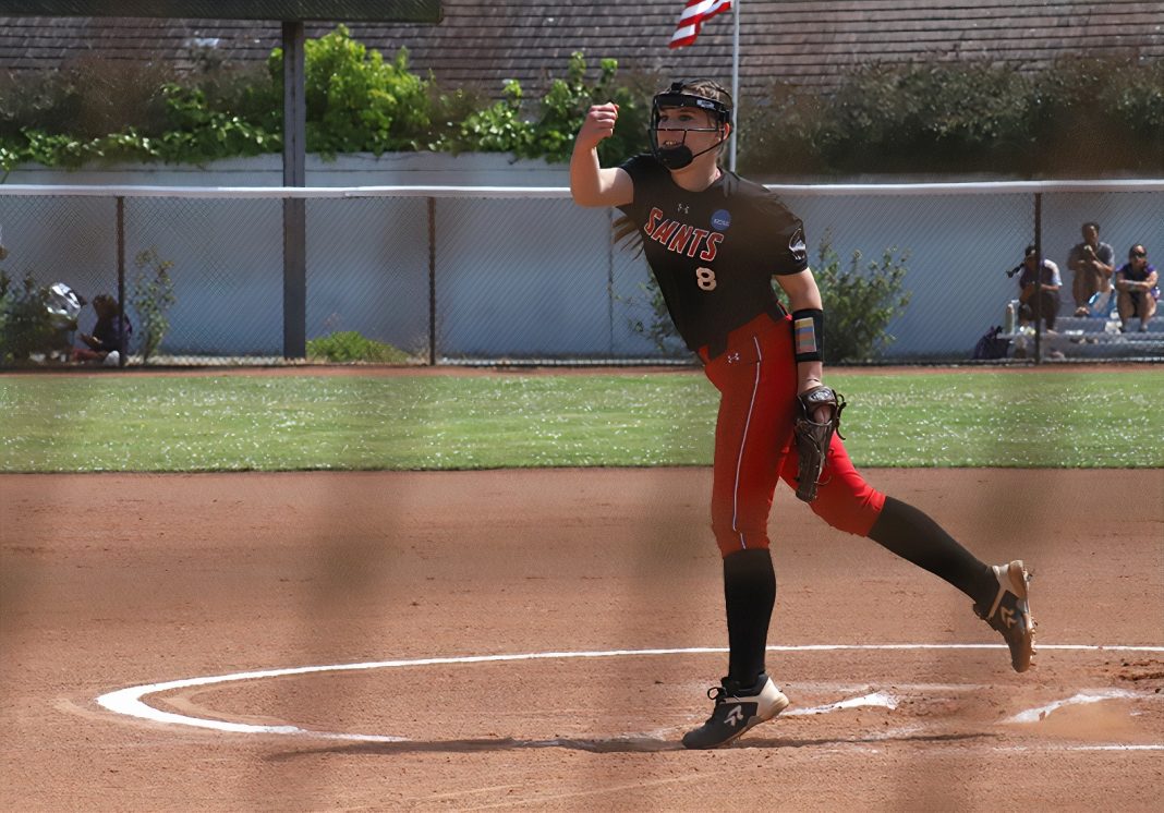 Saint Martin's University softball player in a red and black uniform. She in side a white-chalk outlined circle on red dirt with her arm outstretch and a leg back, as fi she had just thrown a ball. her other hand has a catcher's mitt on