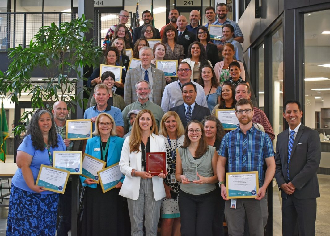 A large group of Thurston County employees holding award plaques and posing for a photo on stairs