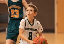 little boy running on a basketball court with a basketball in an Evergreen Christian School jersey. Another boy in a different green uniform is behind him