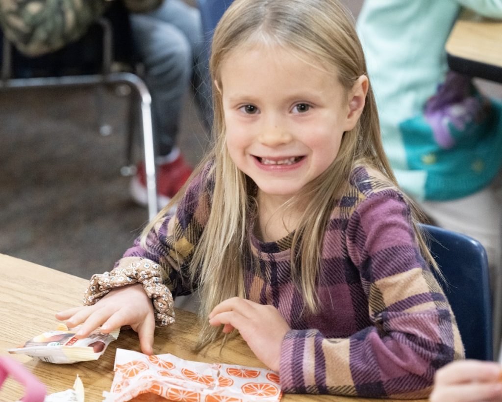 a little girl sitting at a desk smiling at the camera at Evergreen Christian School, a private school in Olympia