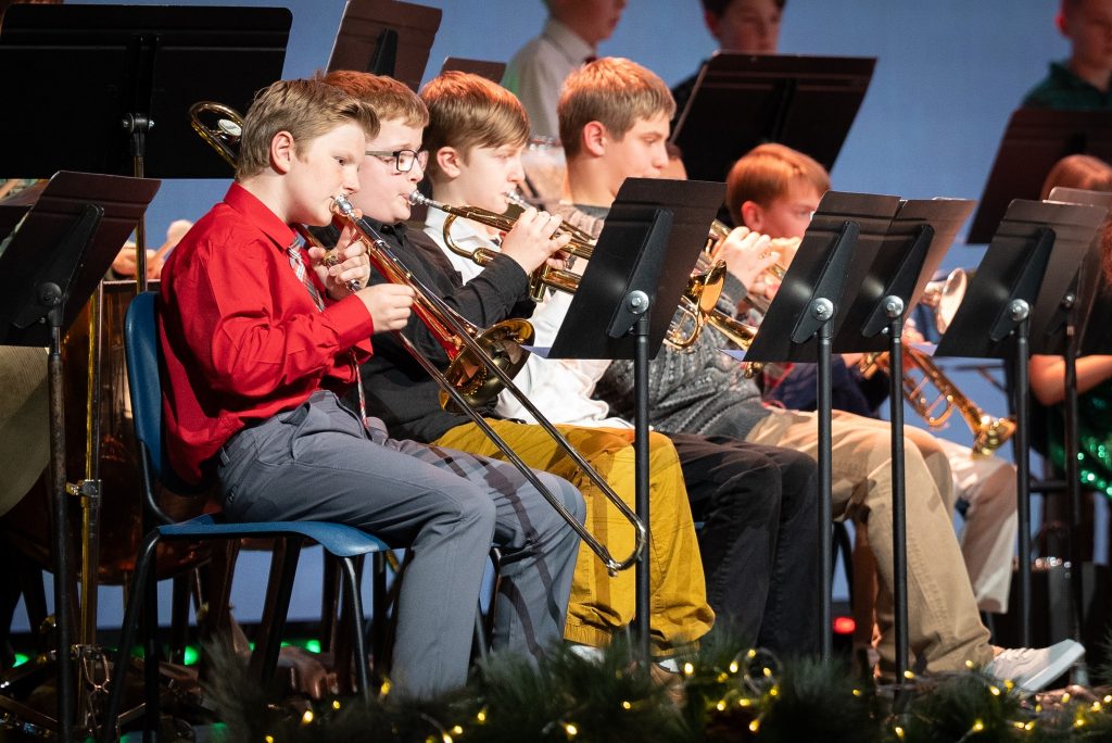 a bunch of young kids sitting in chair with music holders in front of them. All of them are playing trumpets
