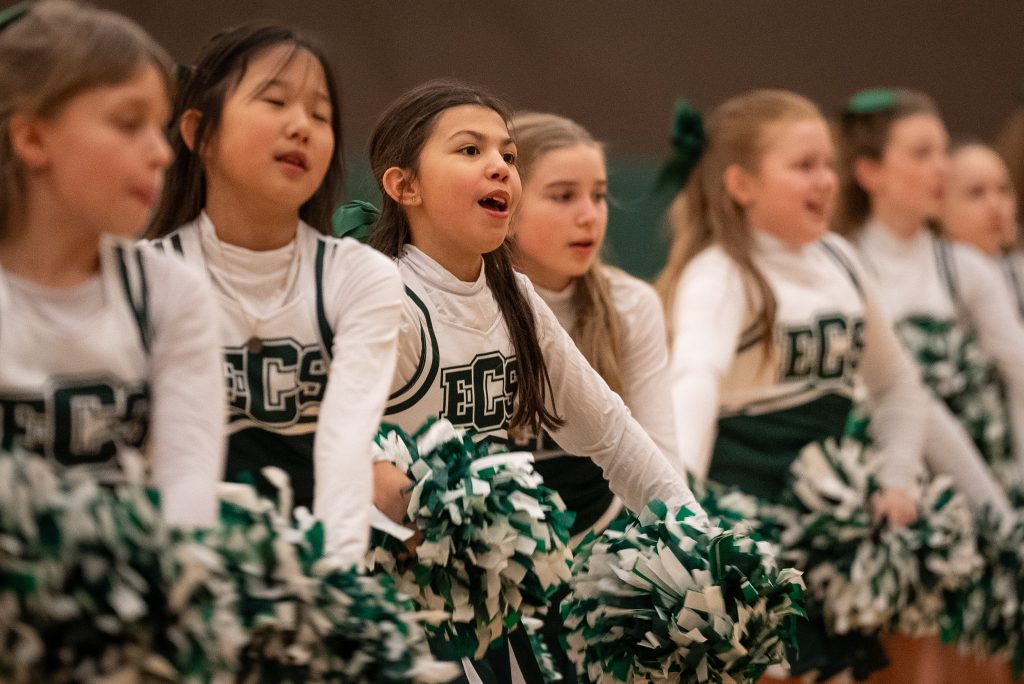 Little girls in a row in Evergreen Christian School cheerleading uniforms with green and white pom poms