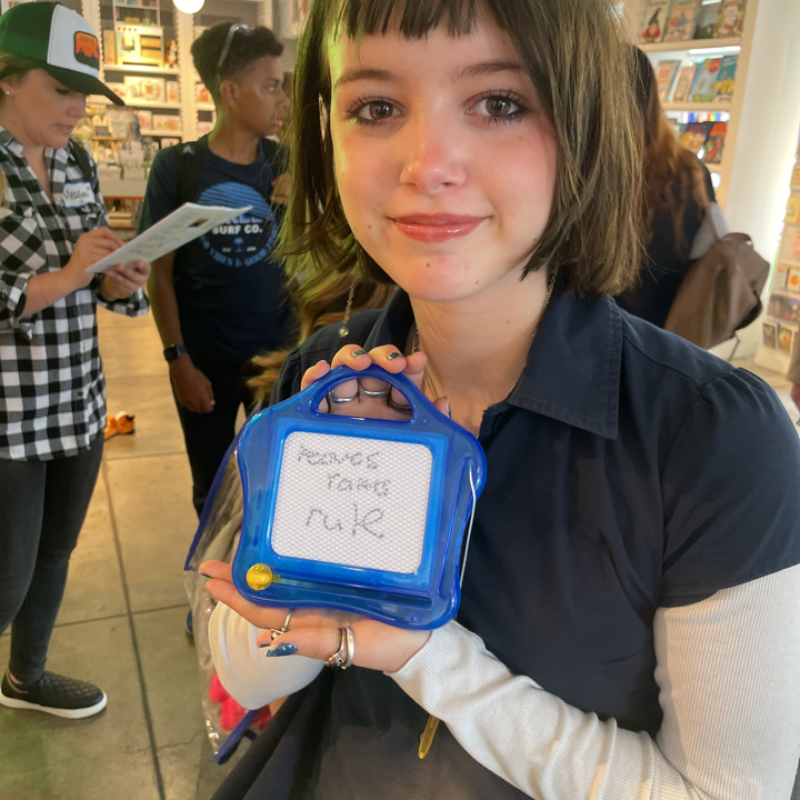 a middle school student holds up a tiny etch-a-sketch with something illegible written on it