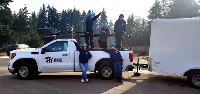 south sound habitat for humanity boeing grant nonprofit affordable homes (1) three people stand in the back of the South Puget Sound Habitat for Humanity's new truck, with two people standing on ground next to it.