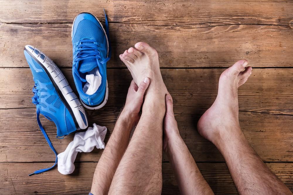 a person's feet and legs are pictures, they are massaging one of thier feet with both hands. A pair of blue sneakers and socks are next to the feet.
