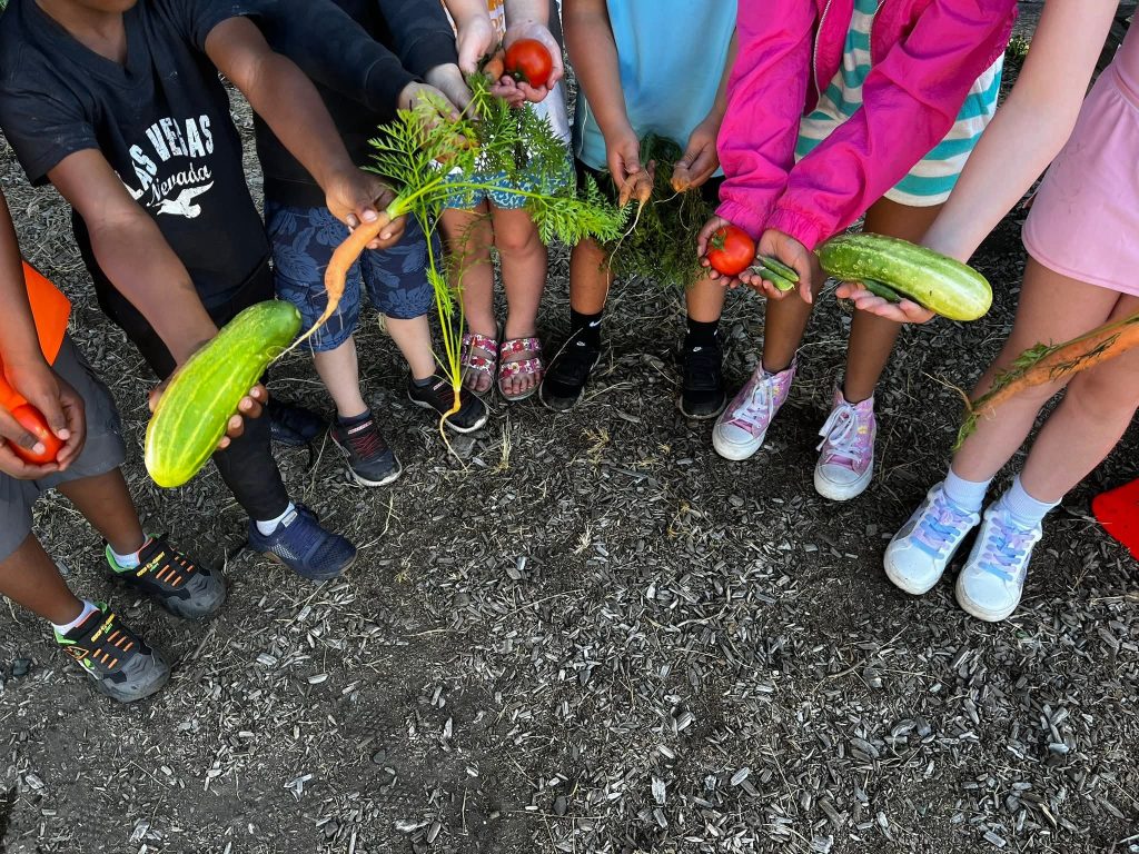 Kids in a semi-circle holding different vegetables in their out stretched hands.