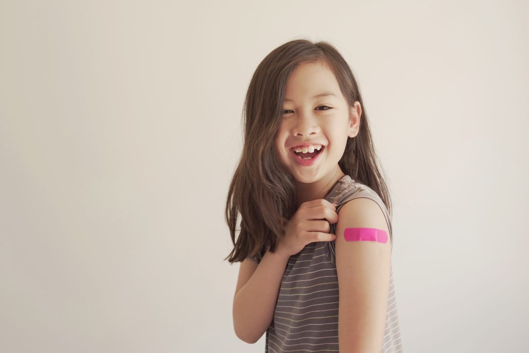 Young girl showing her arm with pink bandage after got vaccinated or inoculation, child immunization, covid delta vaccine concept