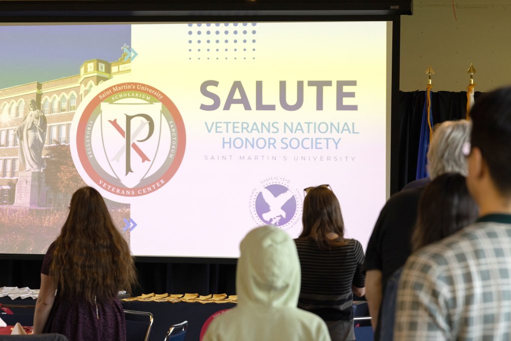 People stand in front of a large screen that says Salute Veterans National Honor Society