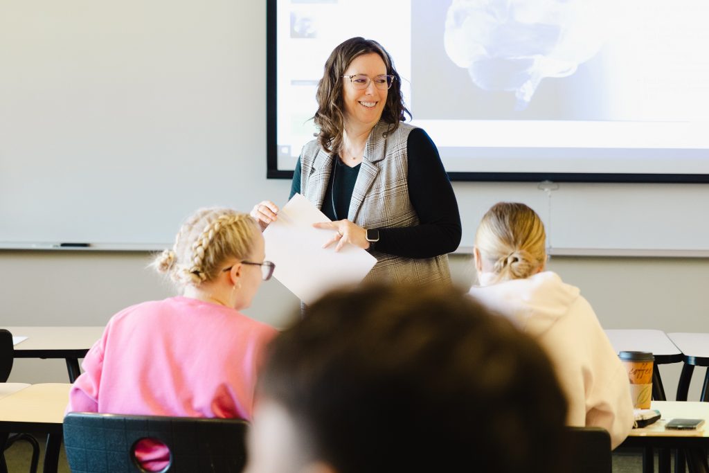 a teacher at Saint Martin's University stands in front of her class, smiling and holding papers