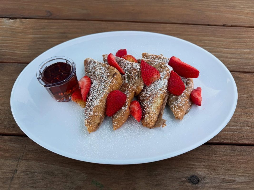 four slices of french toast cut into triangle with strawberries and a small cup of syrup