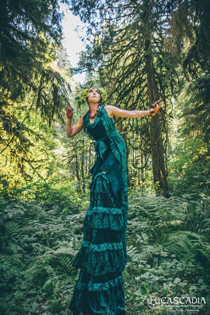 a woman on stilts in a green velvet dress in a forest